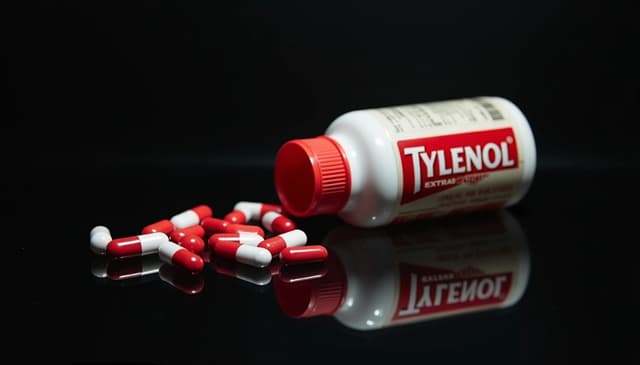 Tylenol Extra Strength bottle tipped over with red-and-white capsules on a glossy black surface—acetaminophen pain reliever product image